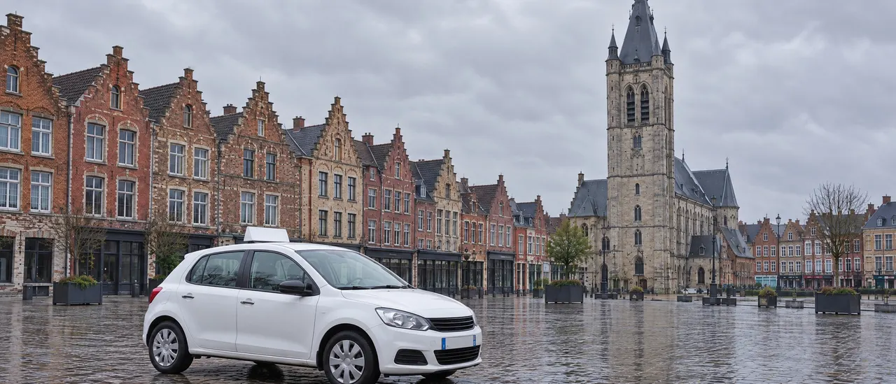 Voiture blanche à double commande garée sur les pavés de la Grand-Place de Béthune, maisons à pignons et beffroi en arrière-plan